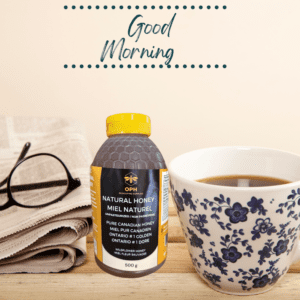 Squeezable 500 g honey jar beside a floral cup and glasses on a wooden table with "Good Morning" backdrop.